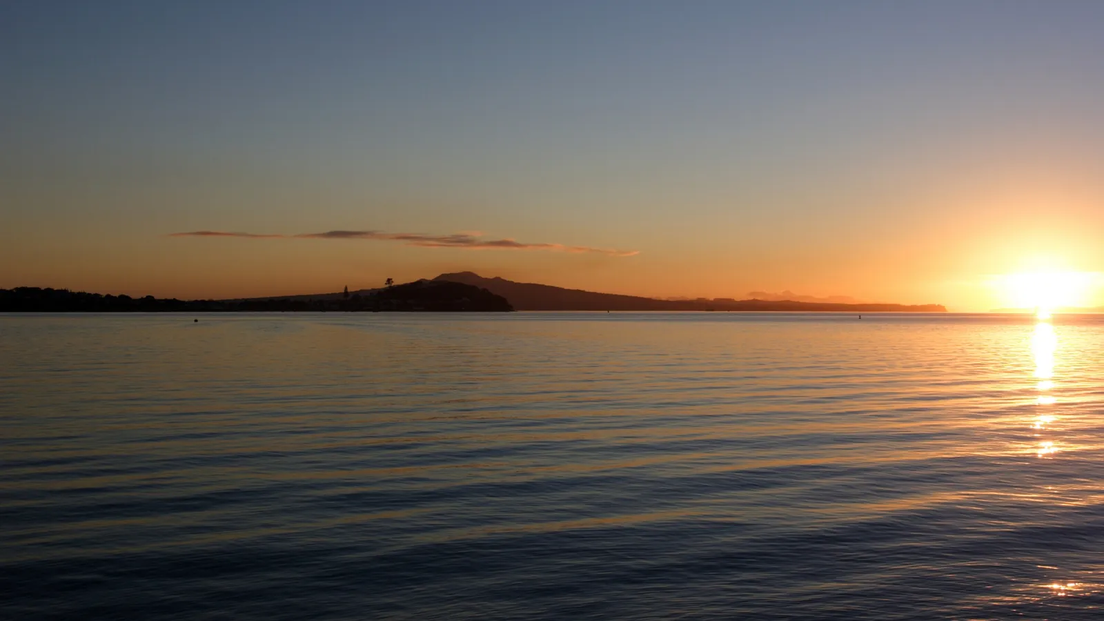 A sunset over a tranquil body of water, casting a warm, golden light across the scene.