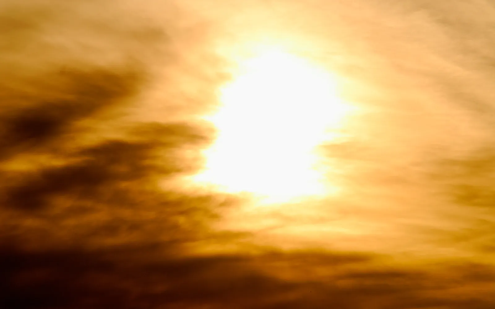 A bright, glowing sun is partially obscured by dark, wispy clouds, creating a dramatic sky.