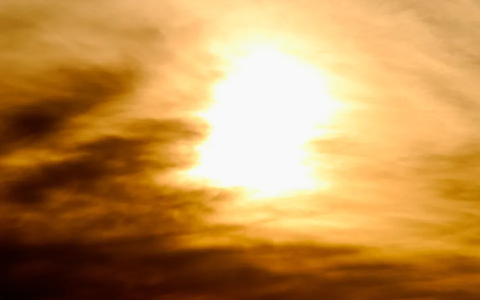 A bright, glowing sun is partially obscured by dark, wispy clouds, creating a dramatic sky.