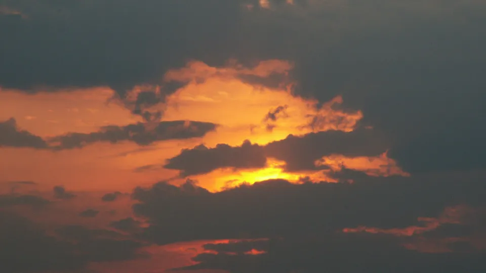 A dramatic sunset with fiery orange and yellow light illuminating dark clouds.