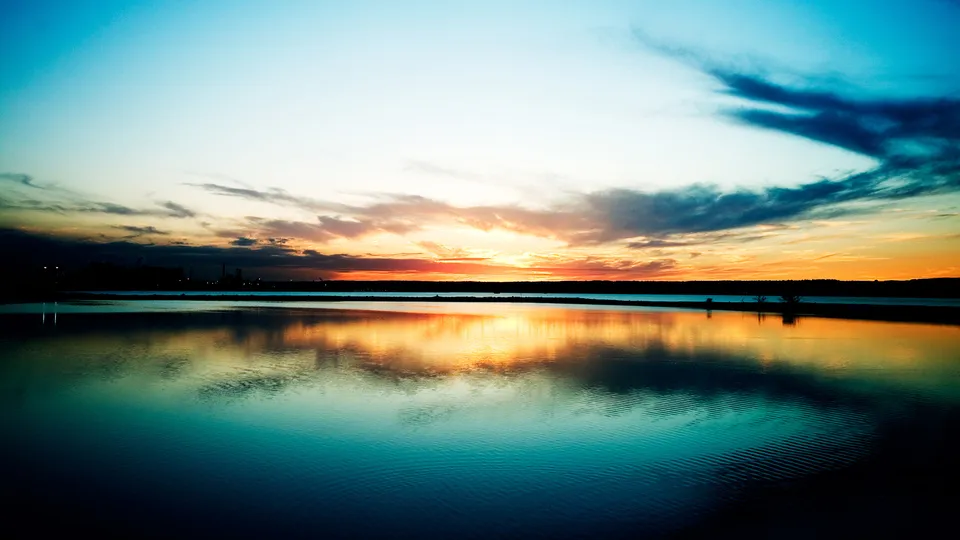 Fiery sunset colors are reflected in the teal water of a calm ocean.