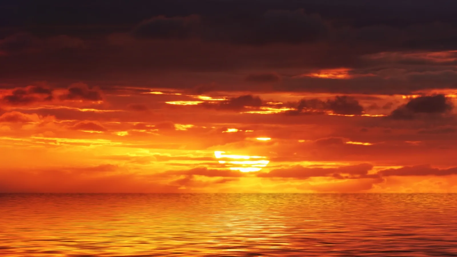 The sun dips below the horizon, casting a fiery glow across the sky and water.