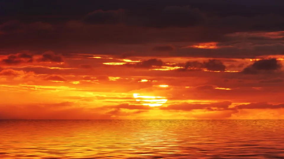The sun dips below the horizon, casting a fiery glow across the sky and water.