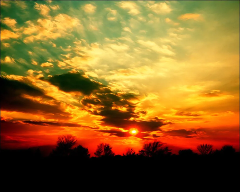 A vibrant sunset with intense orange and red hues, casting a silhouette of trees against the horizon.