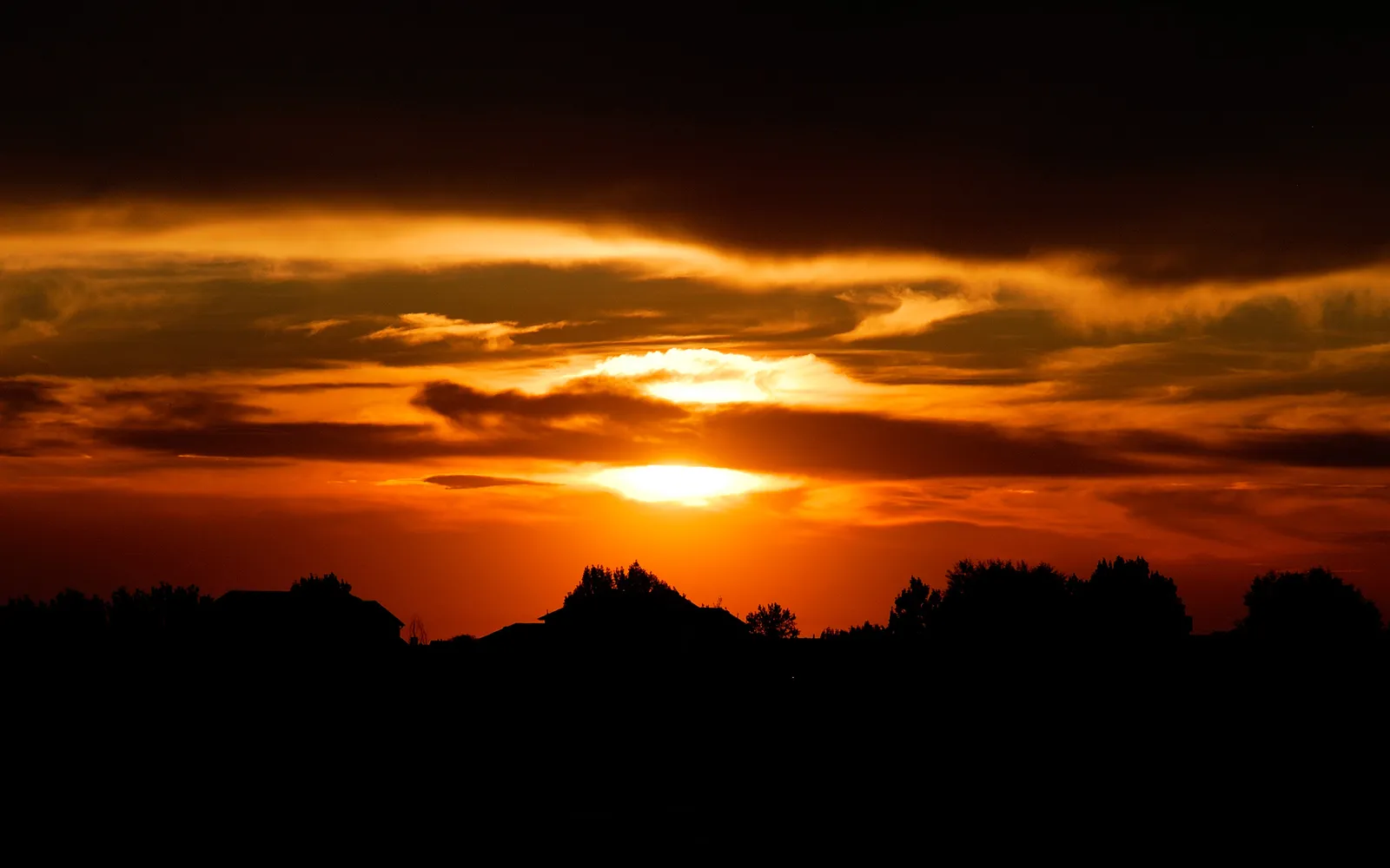 A vibrant sunset with intense orange and yellow hues illuminating the clouds above a dark, silhouetted landscape.