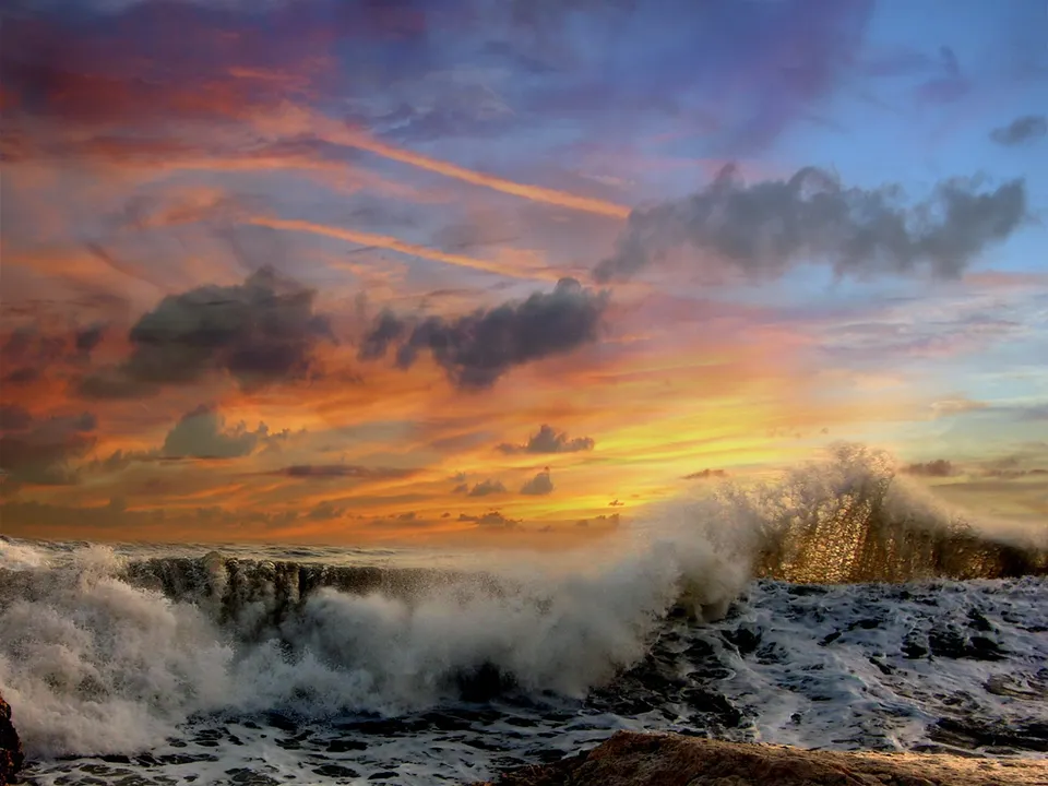 A vibrant sunset sky with orange and pink hues over powerful ocean waves.