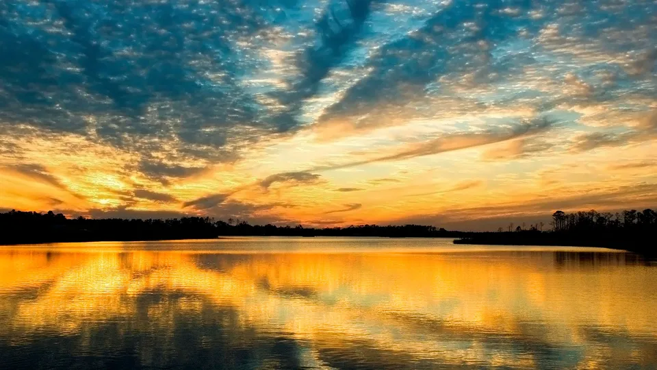 A dramatic sunset with fiery oranges and blues reflects brilliantly on a still lake.