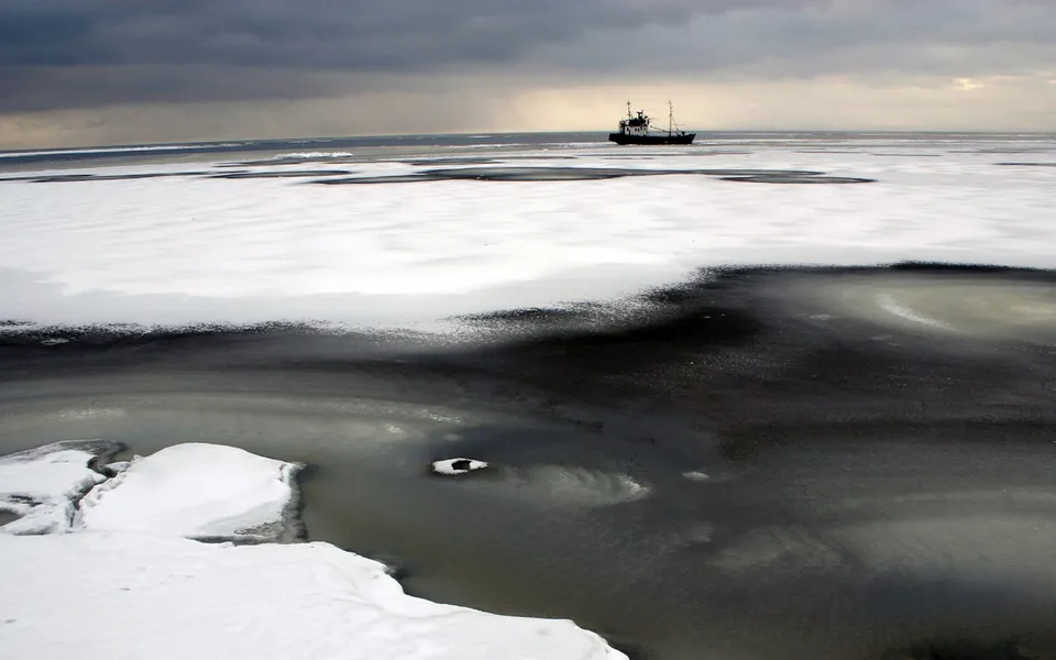 A fishing boat sails on a partially frozen sea under a dramatic, cloudy sky.