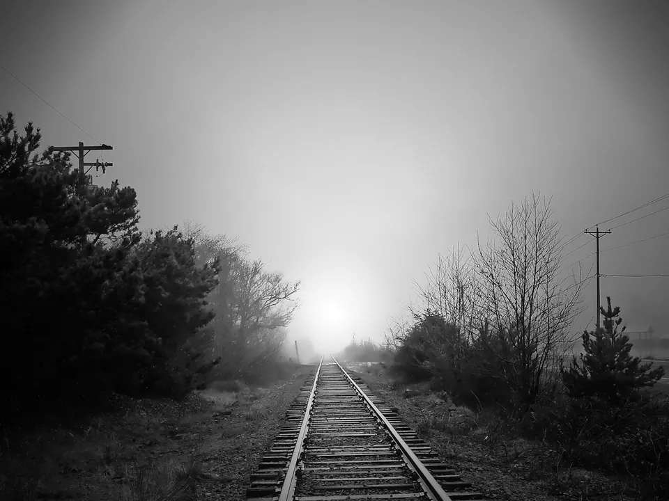 A black and white image of train tracks disappearing into a thick fog.