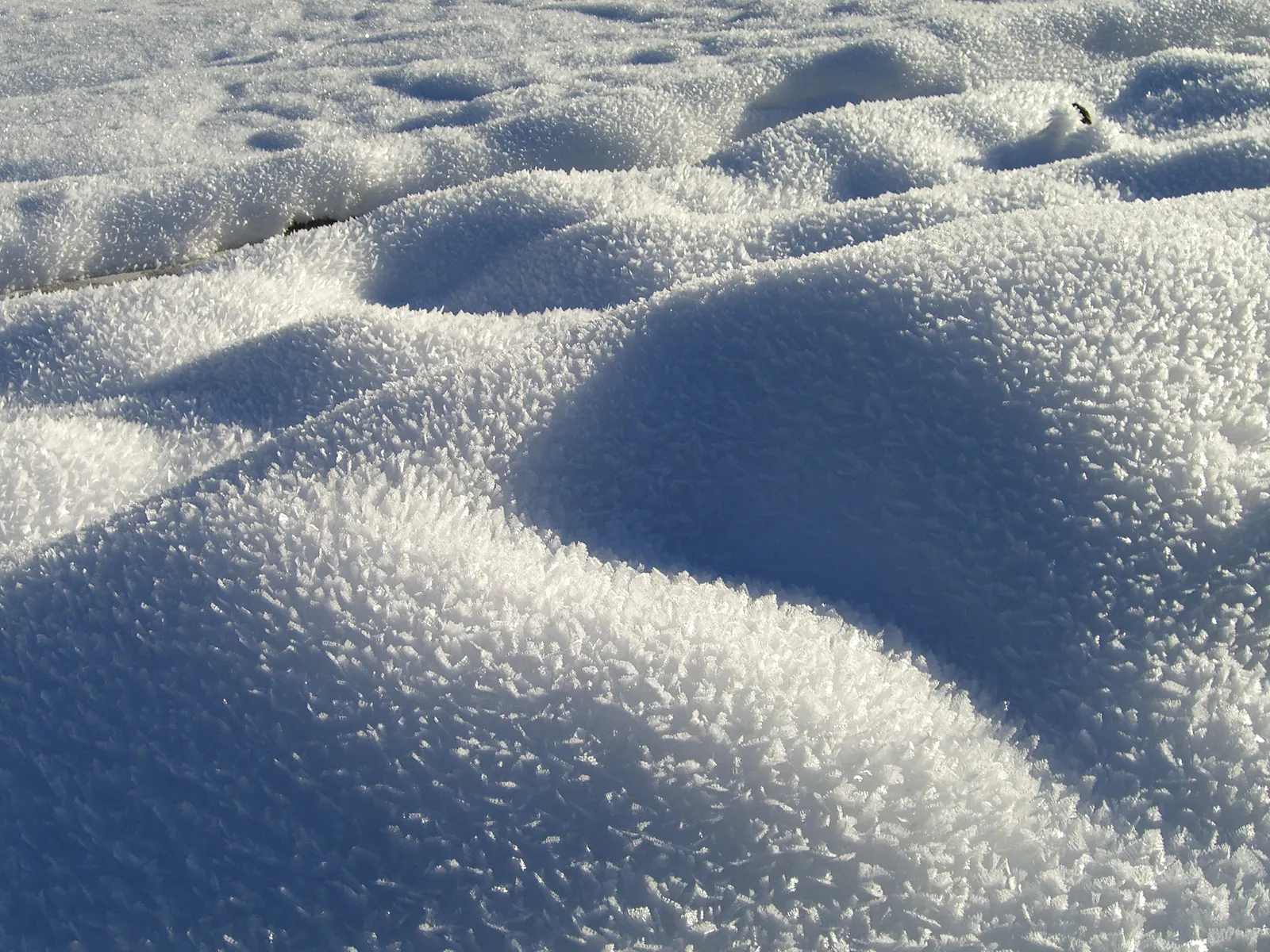 Close-up of snowdrifts covered in delicate ice crystals, casting shadows.