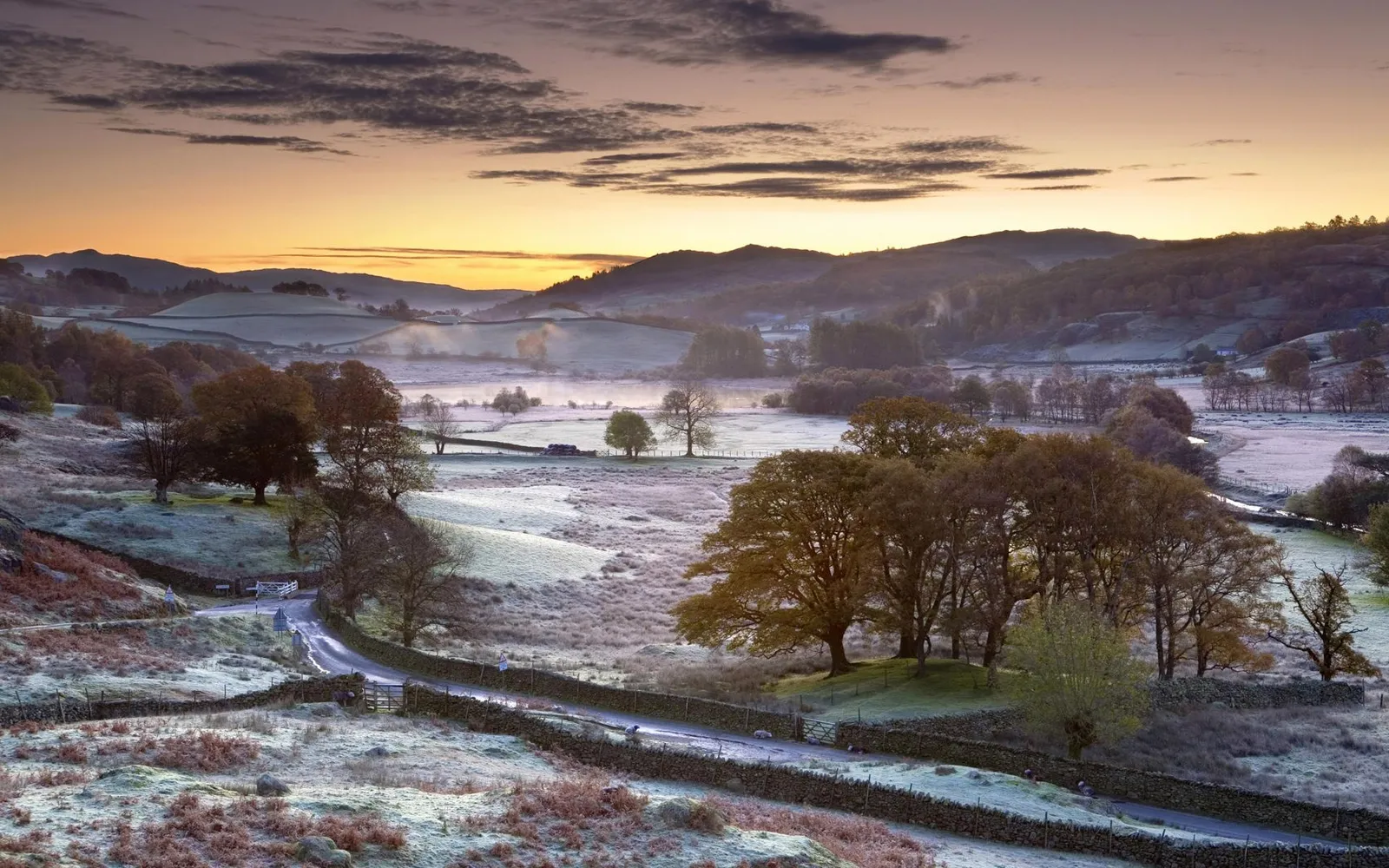 A misty valley with frost-covered fields and rolling hills at sunrise.