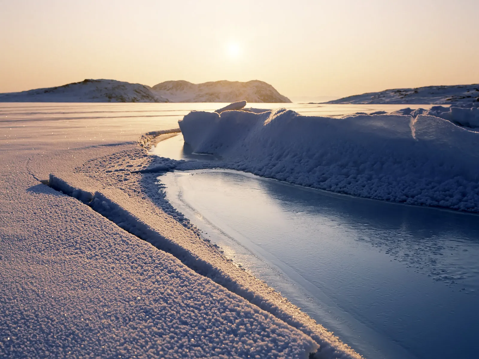 A frozen lake with cracks and ice formations under a pale sky.