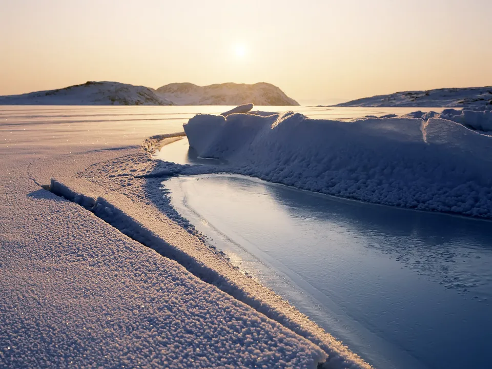 A frozen lake with cracks and ice formations under a pale sky.