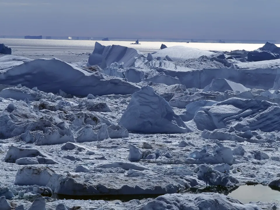 A dense field of icebergs and ice formations covers the frozen sea, with a low sun creating a stark landscape.