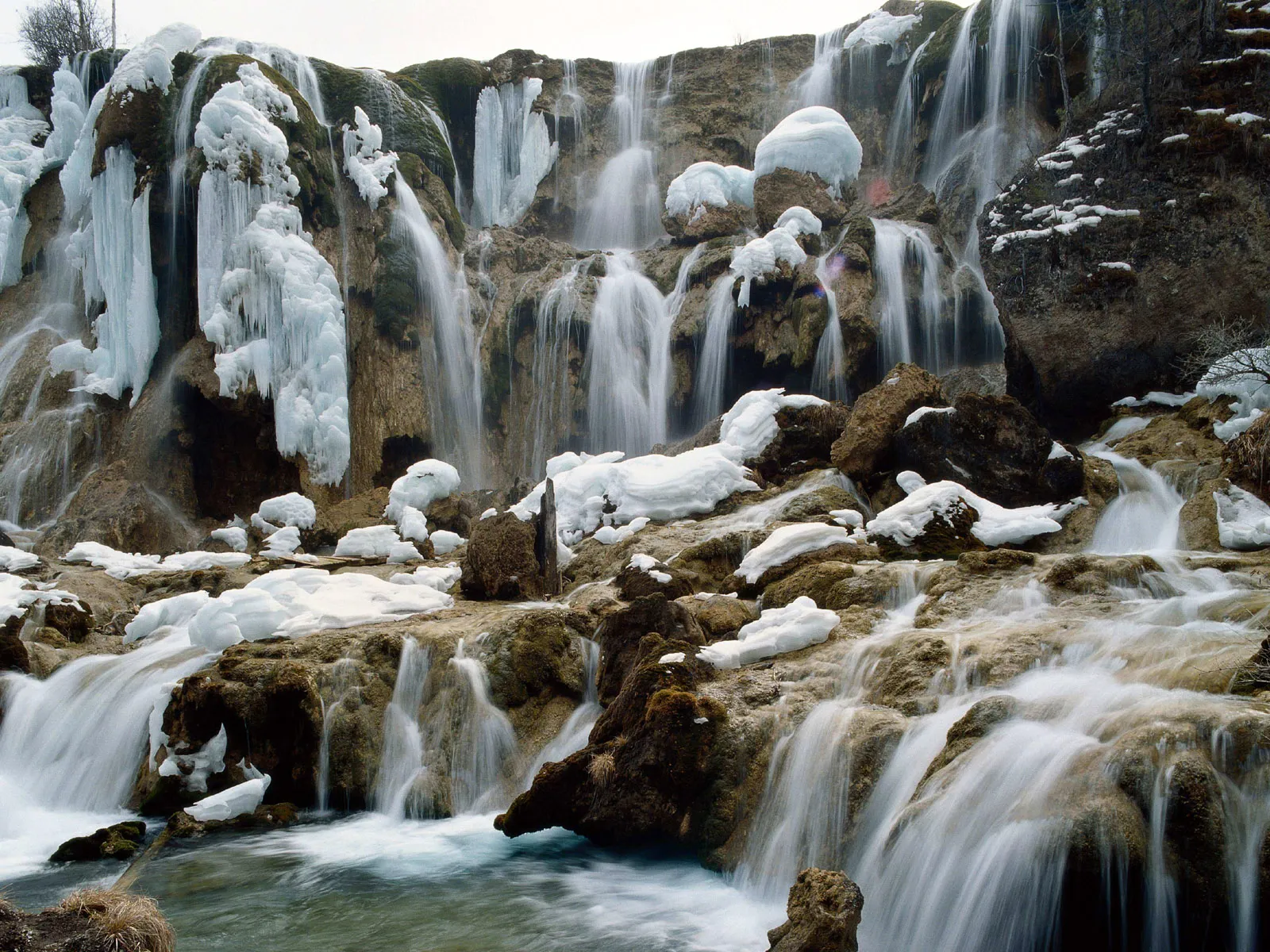 A multi-tiered waterfall with ice formations and flowing water over rocky terrain.