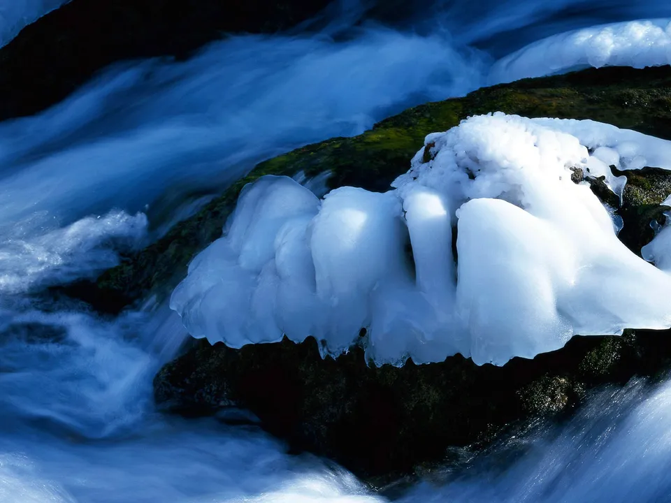 Close-up of ice formations on rocks with water flowing around them.