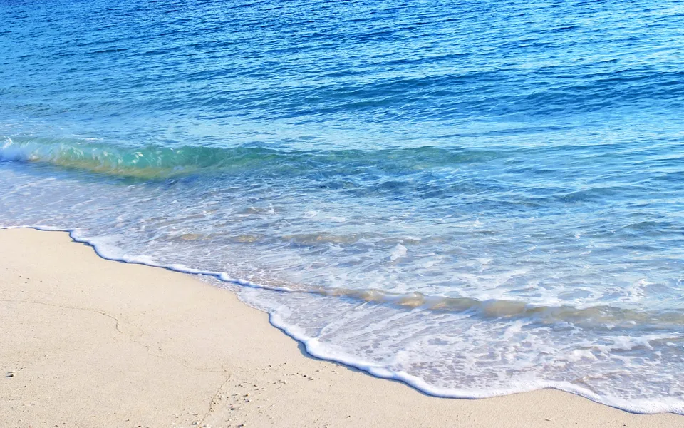 A gentle wave washes onto a sandy beach with clear blue water.