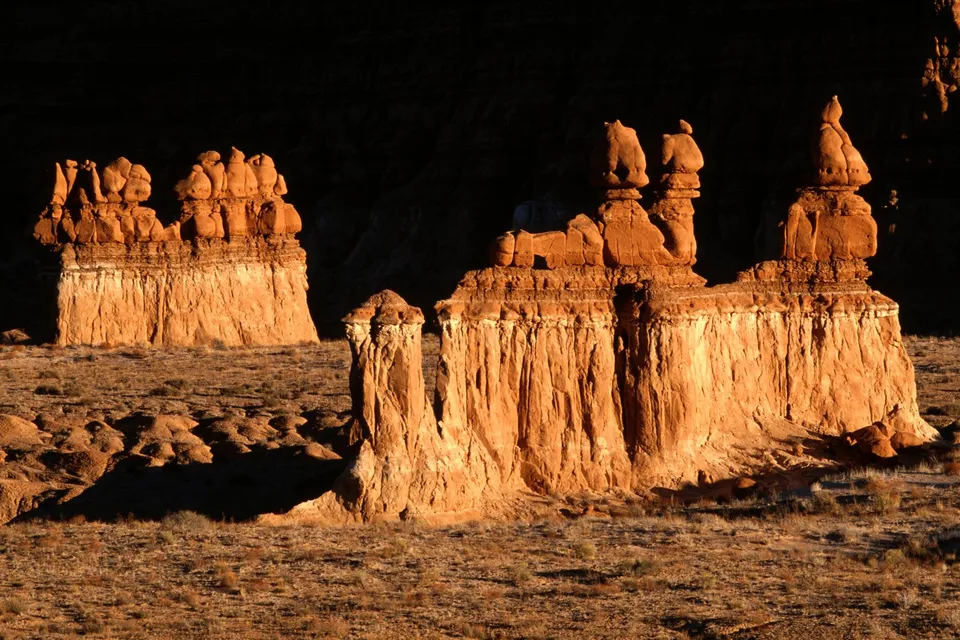 Tall sandstone hoodoos glow orange in the setting sun in Goblin Valley, Utah.