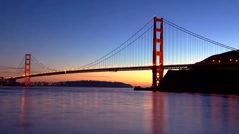 The Golden Gate Bridge illuminated at dusk with its reflection visible in the calm water below.