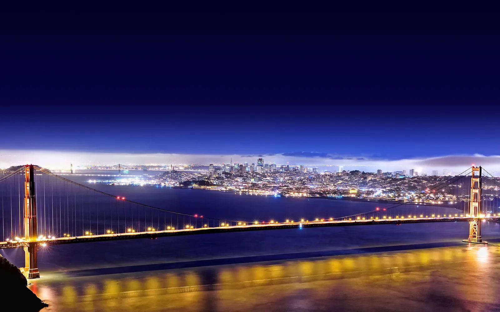 The Golden Gate Bridge is lit up at night with the city skyline in the background.