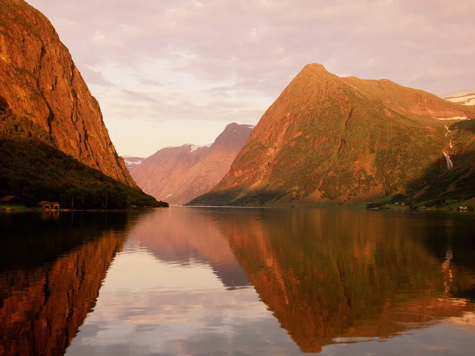 A serene lake reflects golden-hued mountains during the golden hour.