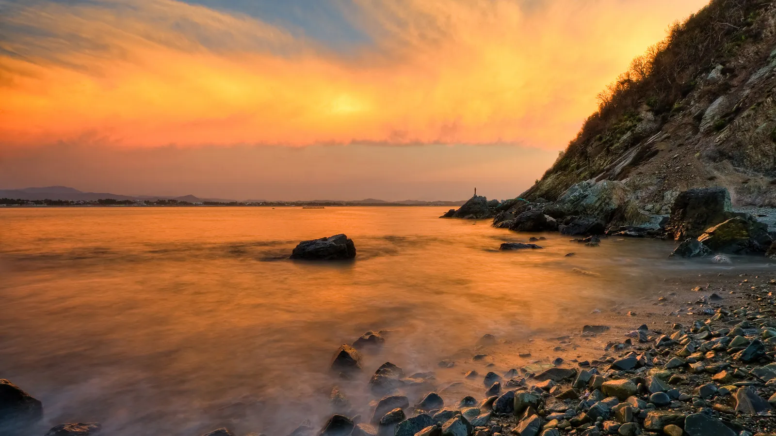 A rocky coastline bathed in the warm glow of a sunset, with calm water and colorful clouds.
