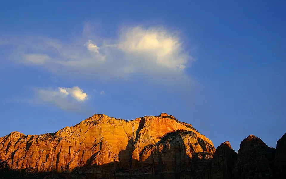 Golden hour light illuminates sandstone cliffs under a blue sky with wispy clouds.