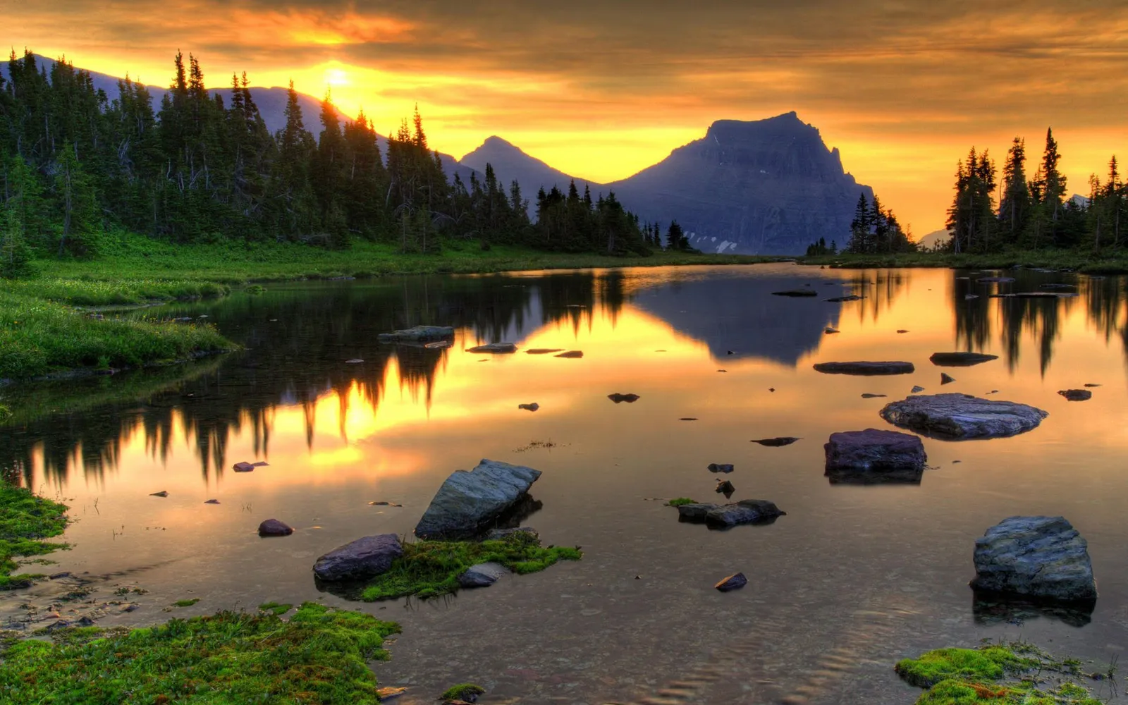 A dramatic sunset or sunrise over a lake with silhouetted mountains.