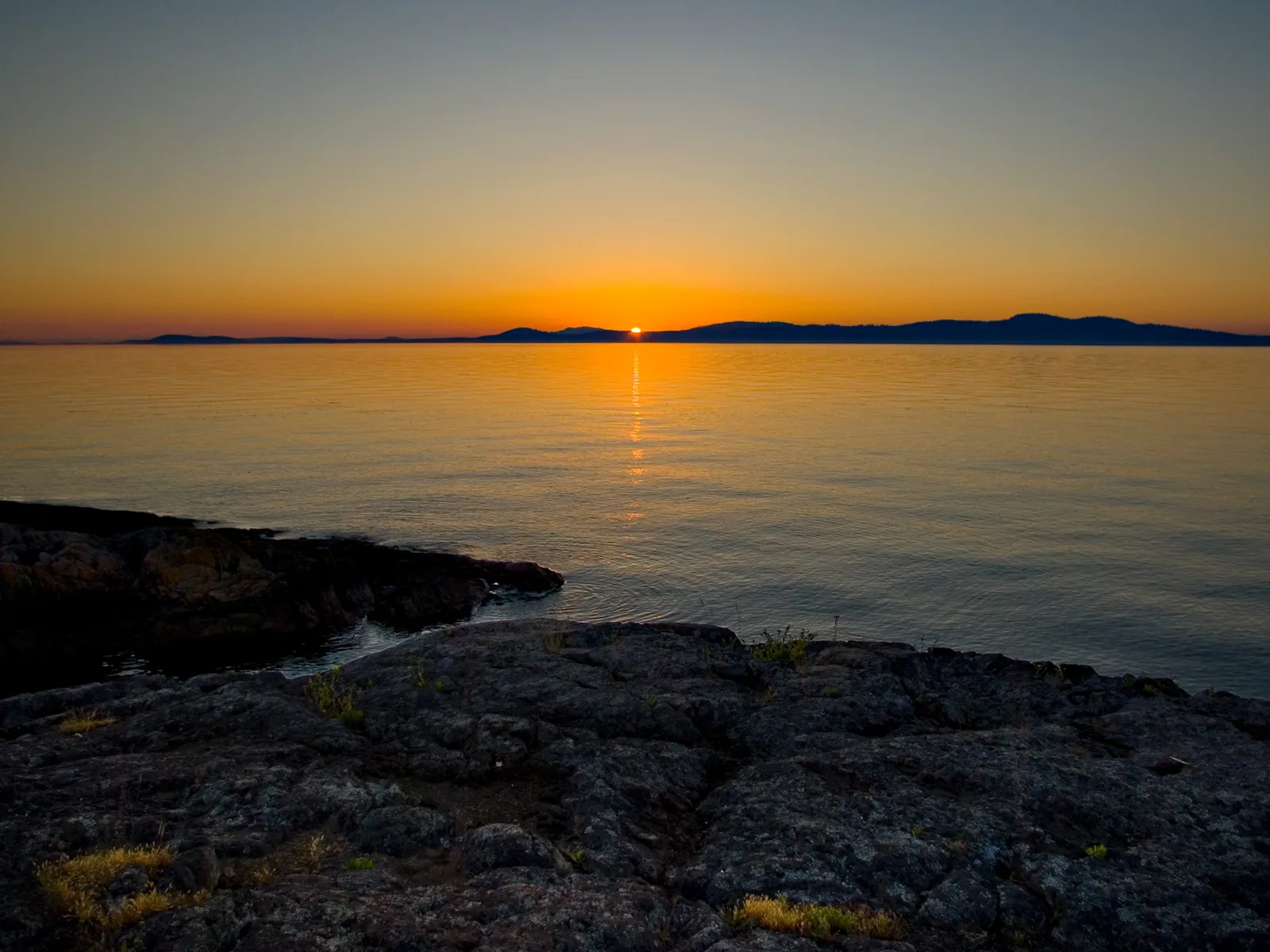 A golden hour sunset over a calm ocean with distant islands on the horizon.