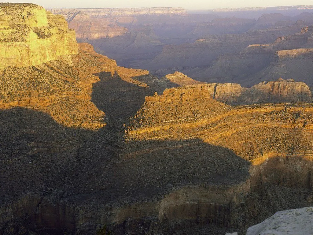 The Grand Canyon is bathed in golden light with long shadows stretching across the canyon floor.