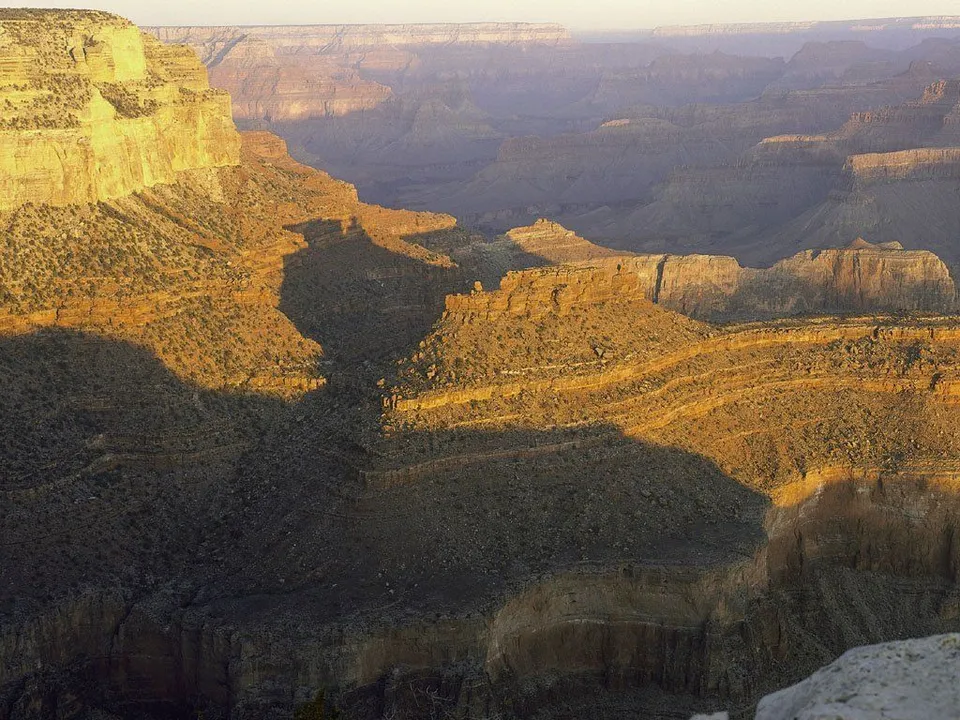 The Grand Canyon is bathed in golden light with long shadows stretching across the canyon floor.