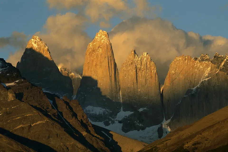 Jagged mountain peaks illuminated by golden sunset light, with clouds in the sky.