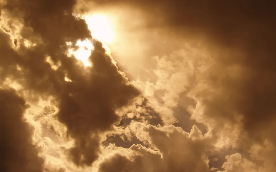 Sunbeams break through dark storm clouds, creating dramatic shafts of light.