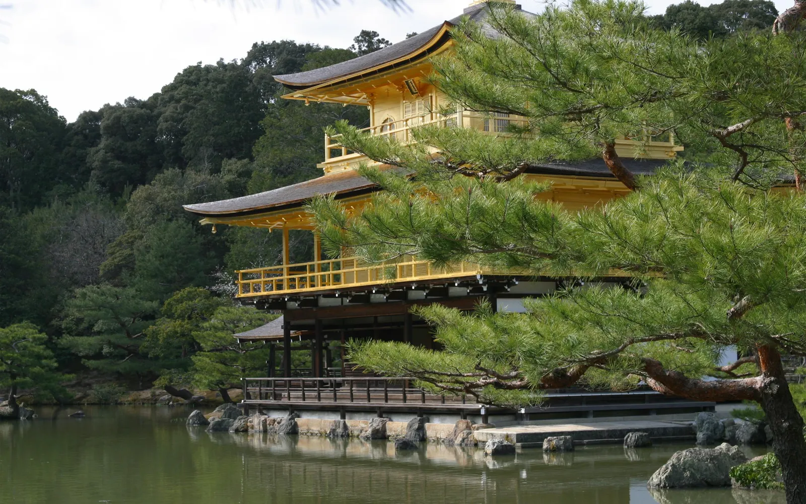 The Golden Pavilion, a Zen Buddhist temple, is reflected in a calm pond, surrounded by lush trees.