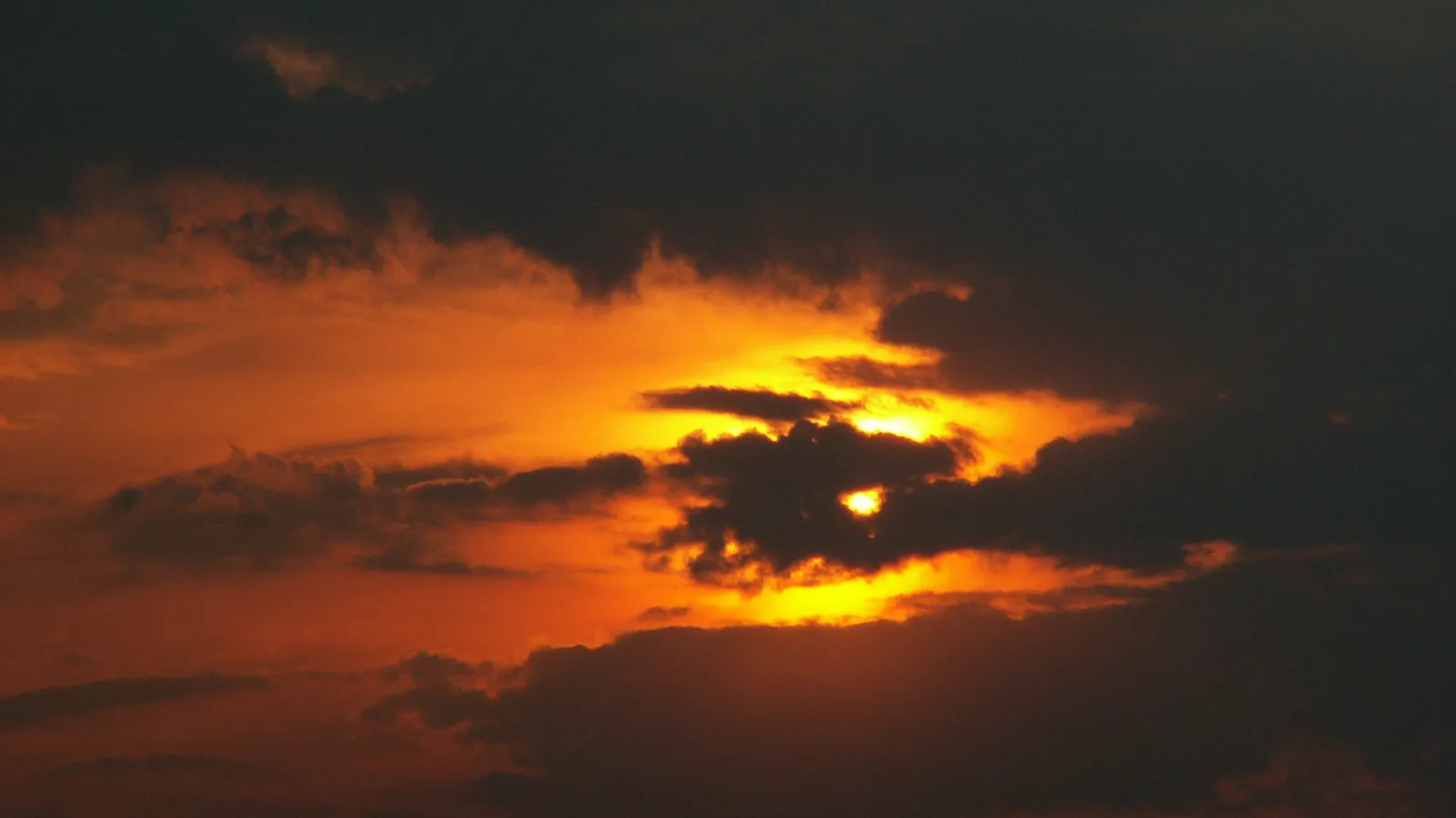 A vibrant sunset casts a golden glow through dark, dramatic clouds in the sky.