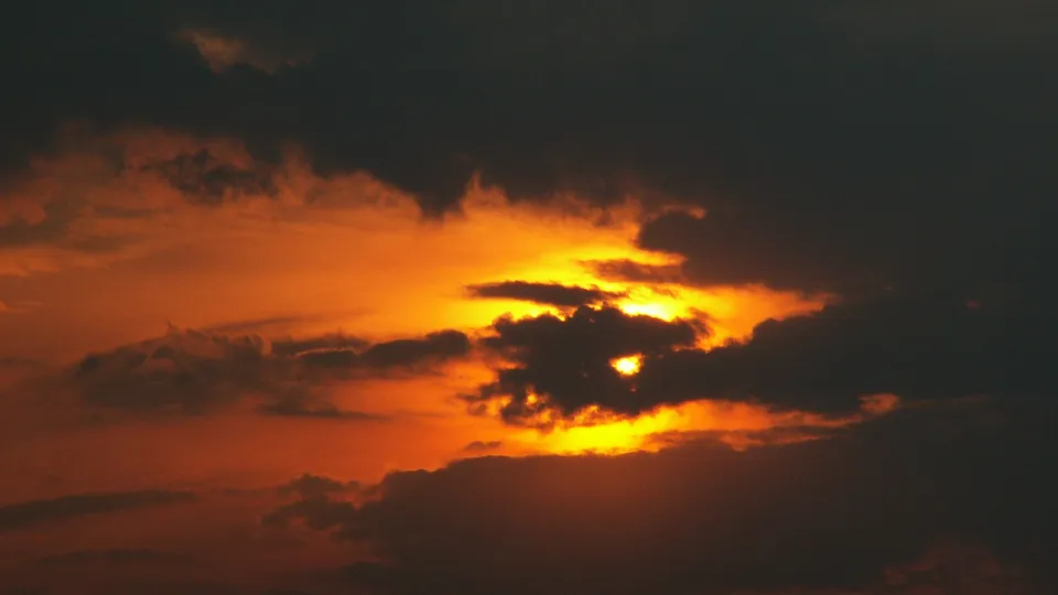 A vibrant sunset casts a golden glow through dark, dramatic clouds in the sky.