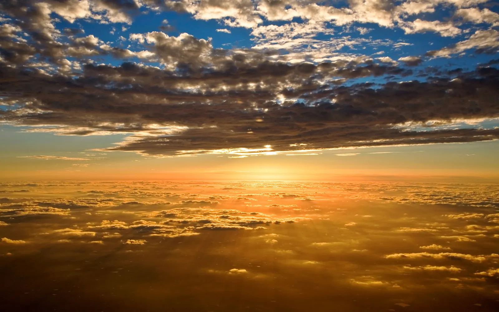 Sunbeams stream through dark clouds over a sea of golden clouds below.