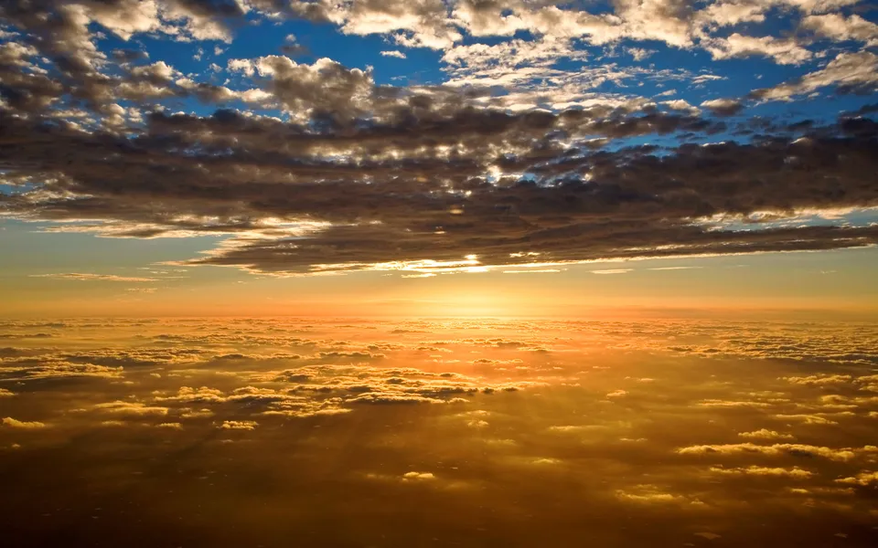 Sunbeams stream through dark clouds over a sea of golden clouds below.