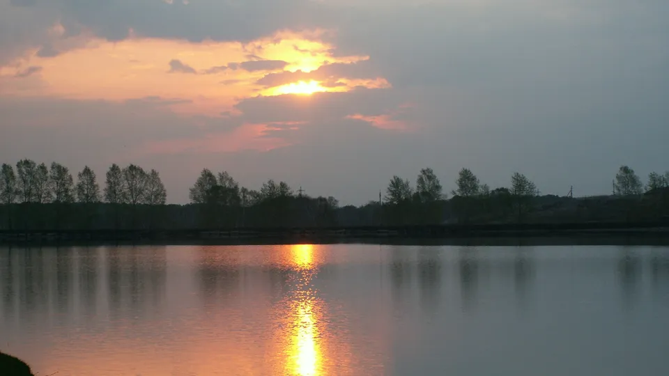 The setting sun casts golden light across the sky and reflects on the still lake surface.