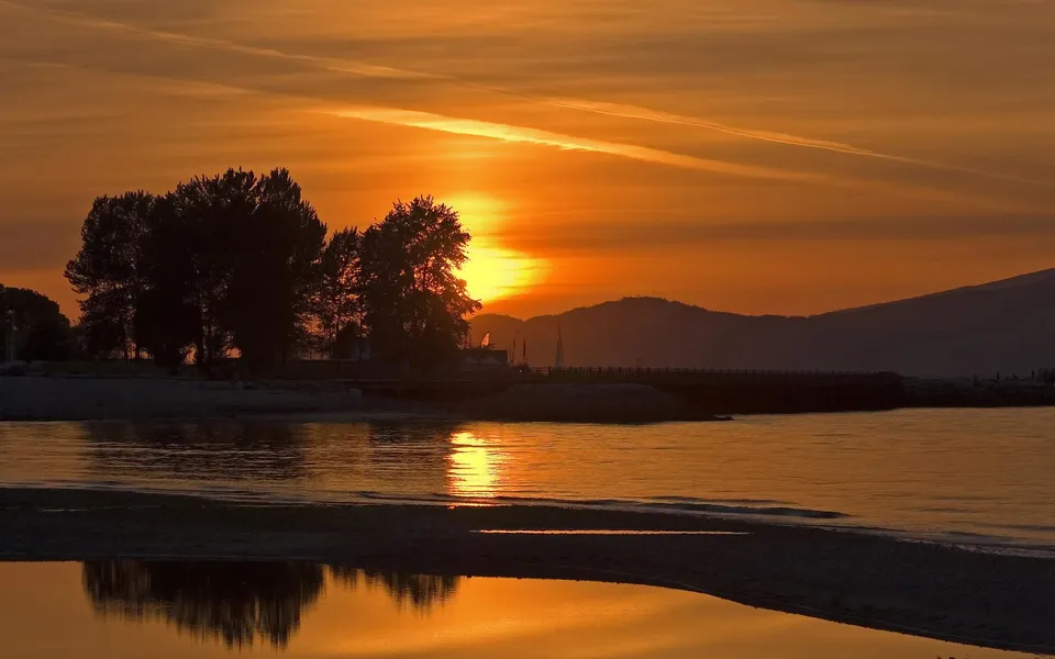 The sun rises over a calm body of water, casting a golden glow on the sky and reflecting on the water's surface.