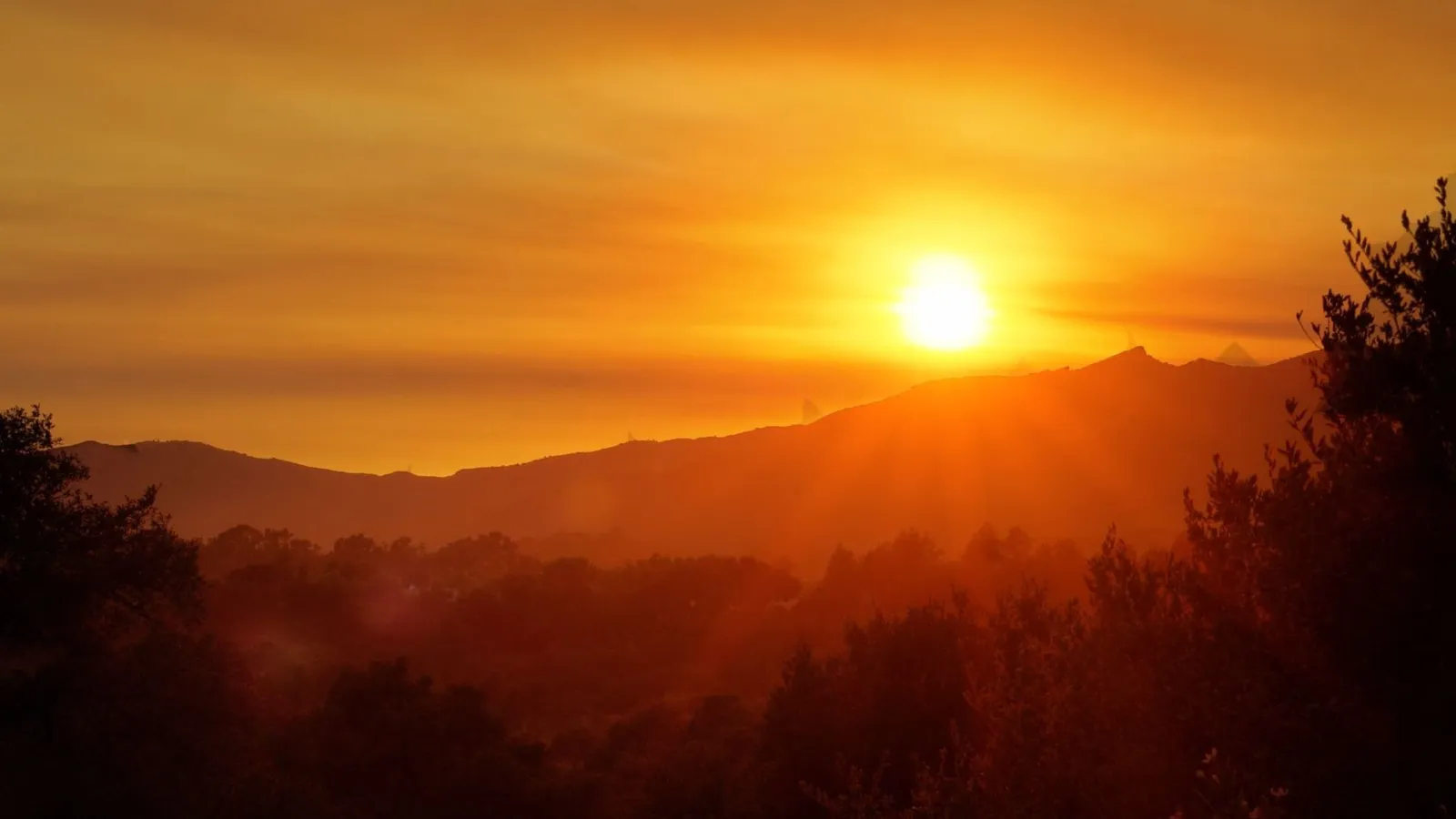 The sun sets behind a range of silhouetted mountains, casting a warm golden glow over the landscape.