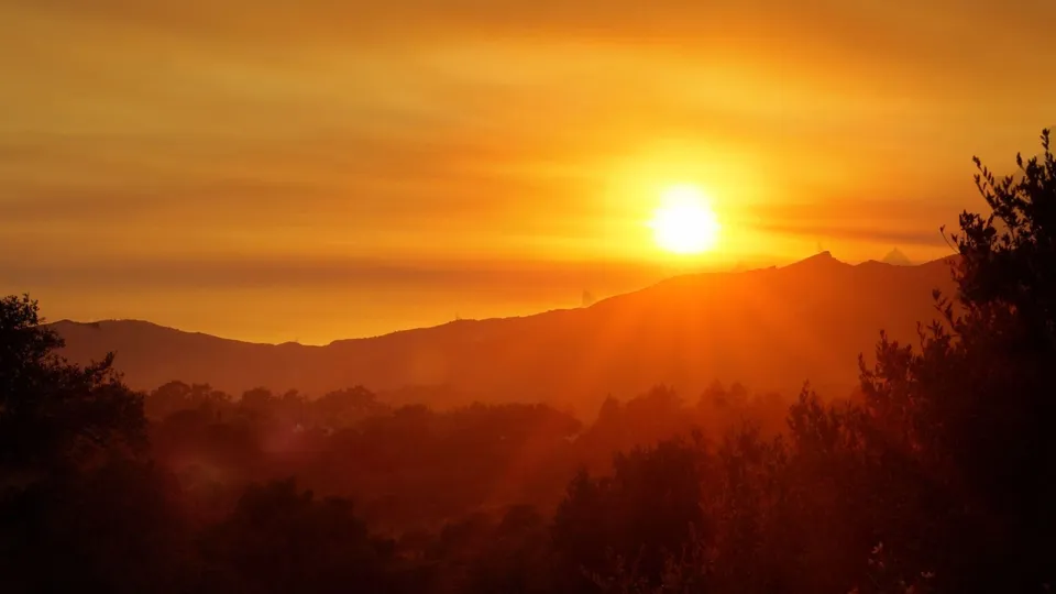 The sun sets behind a range of silhouetted mountains, casting a warm golden glow over the landscape.