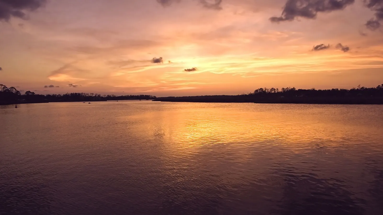A wide river reflects the warm orange and pink hues of a sunset sky with scattered clouds.
