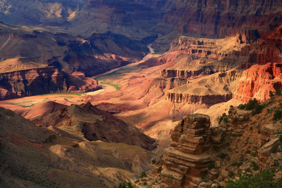 A wide view of the Grand Canyon with the Colorado River winding through it, bathed in warm sunlight.