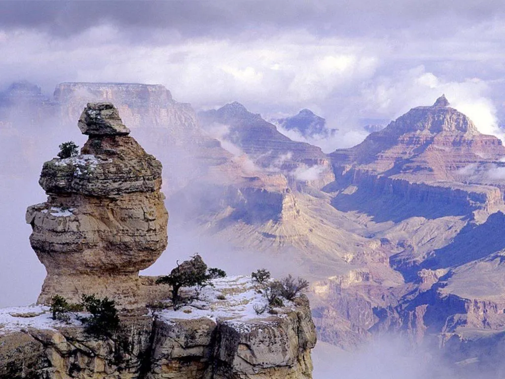 A misty morning view of the Grand Canyon with layered rock formations and clouds.