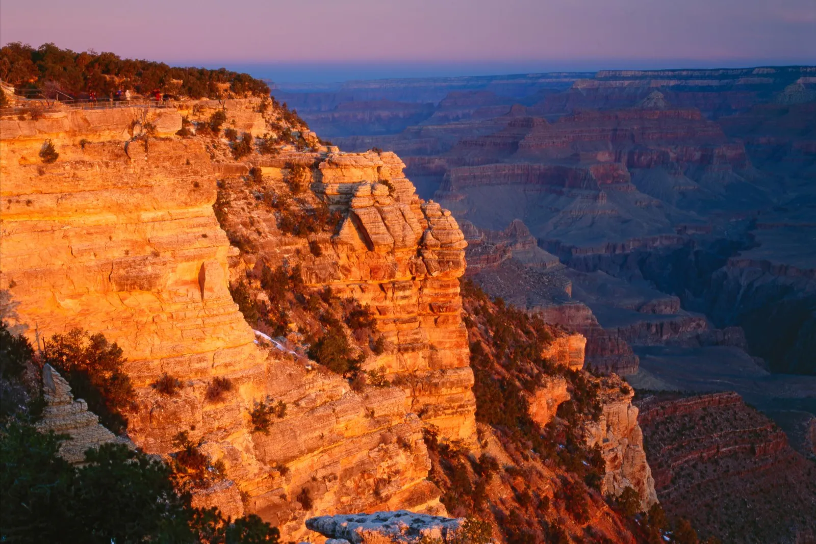 The Grand Canyon illuminated by the warm glow of sunrise, with layers of rock formations stretching into the distance.