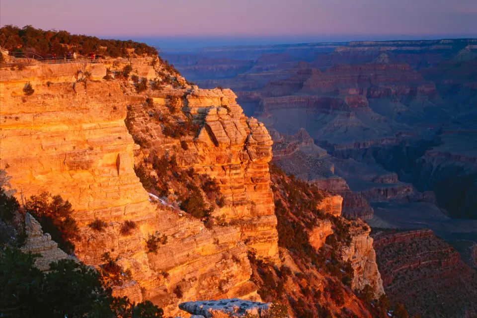 The Grand Canyon illuminated by the warm glow of sunrise, with layers of rock formations stretching into the distance.
