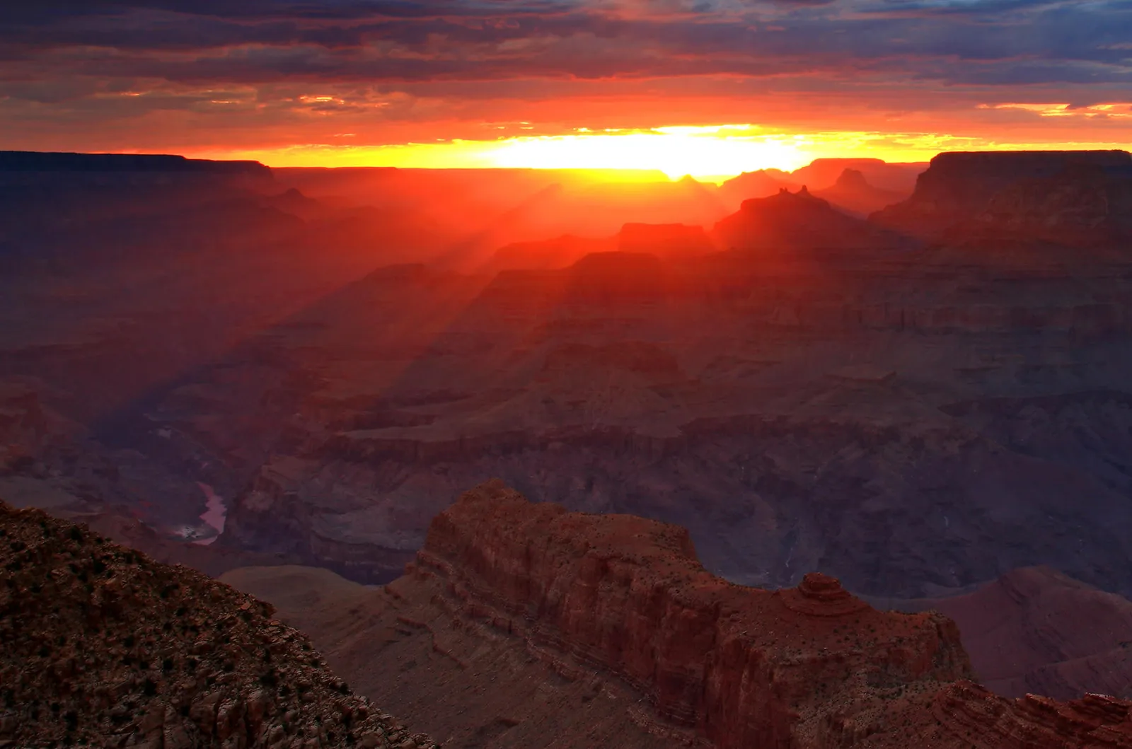 A vibrant sunset casts dramatic rays of light across the layered rock formations of the Grand Canyon.