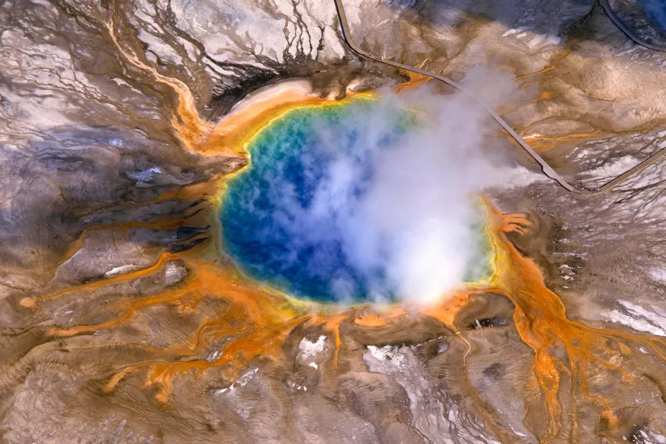 Aerial view of Grand Prismatic Spring showing vibrant blue water surrounded by orange and yellow mineral deposits and steam.