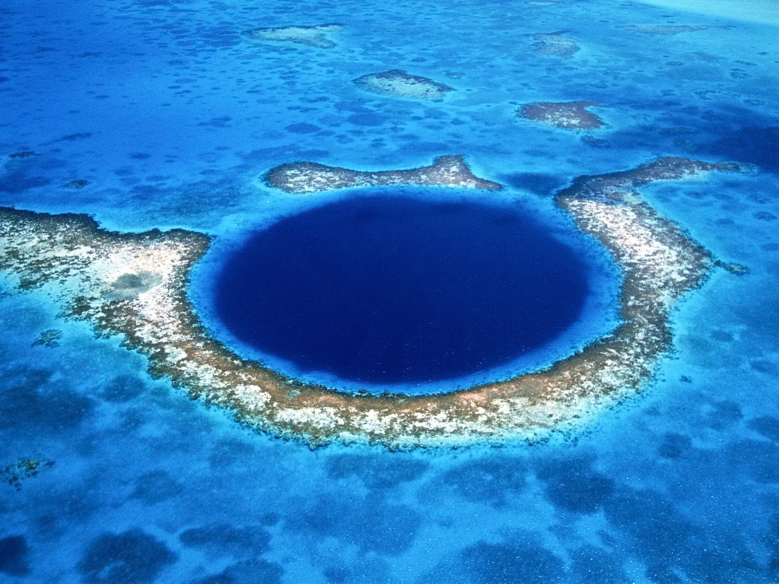 Aerial view of the Great Blue Hole, a deep blue circular sinkhole surrounded by turquoise water and coral reefs.